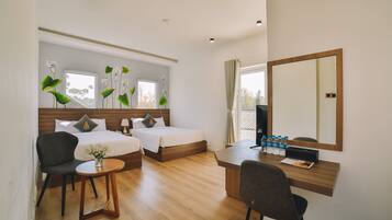 A hotel room with two beds, a desk, a chair, a small table with a vase, and a large mirror.