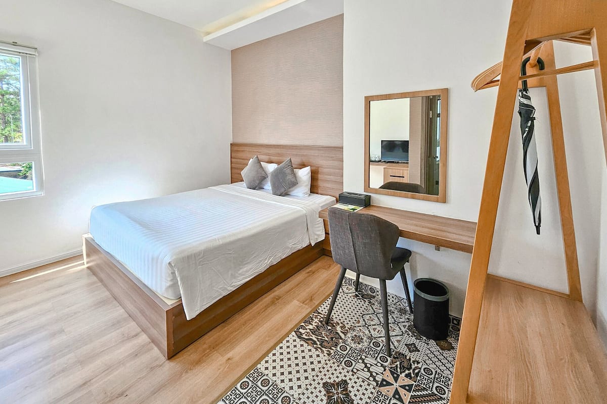 A modern hotel room with a bed, a desk, a chair, a mirror, and a hanging telephone.
