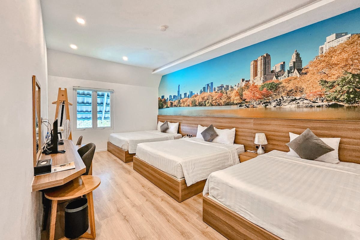 A hotel room with two beds, a desk with a computer, a chair, and a large cityscape mural on the wall.