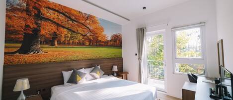 Une chambre à coucher avec un grand lit, un bureau, une chaise, une lampe et un tableau représentant des arbres d'automne.