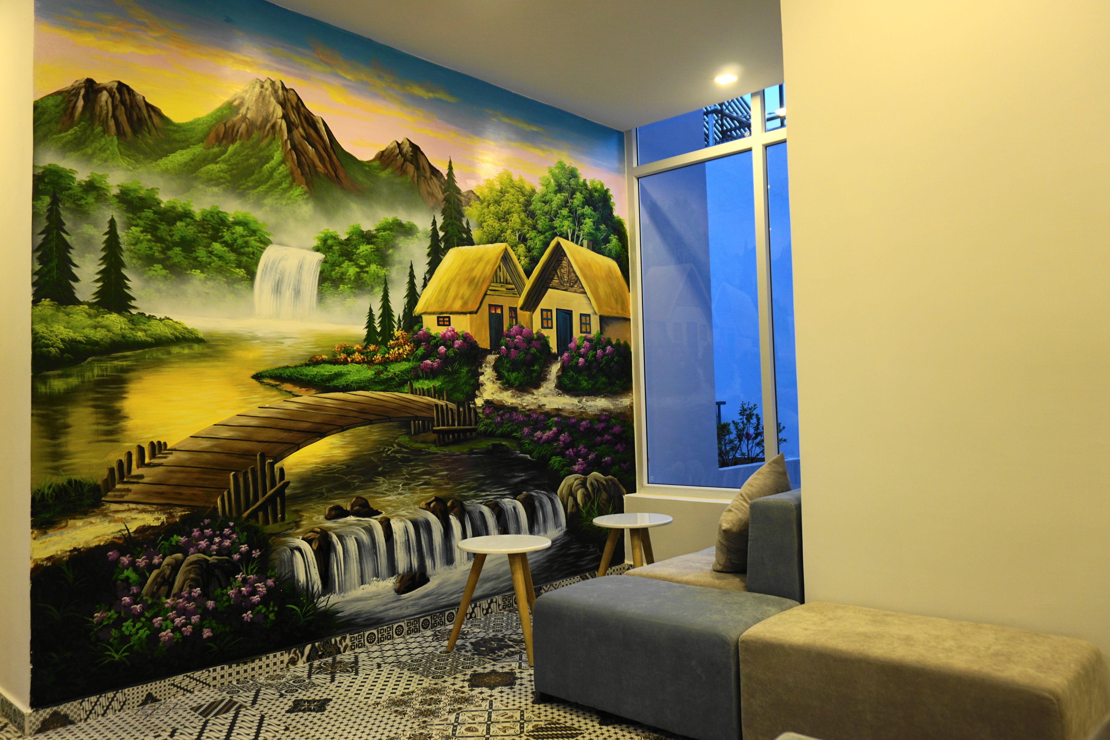 Habitación con un mural de un paisaje que muestra una casa, una cascada y un río. Se ve una ventana con vistas al exterior, un sofá y una mesita.