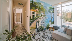 A hotel lobby with a mural of a coastal scene, a patterned floor, and a seating area with a view. -  NATURE LAND 2 - Song Anh Hotel Dalat (Xuan Huong - Da Lat)