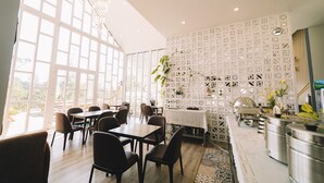 A modern dining area with large windows, a white decorative wall, and a kitchen counter. -  NATURE LAND 2 - Song Anh Hotel Dalat (Xuan Huong - Da Lat)
