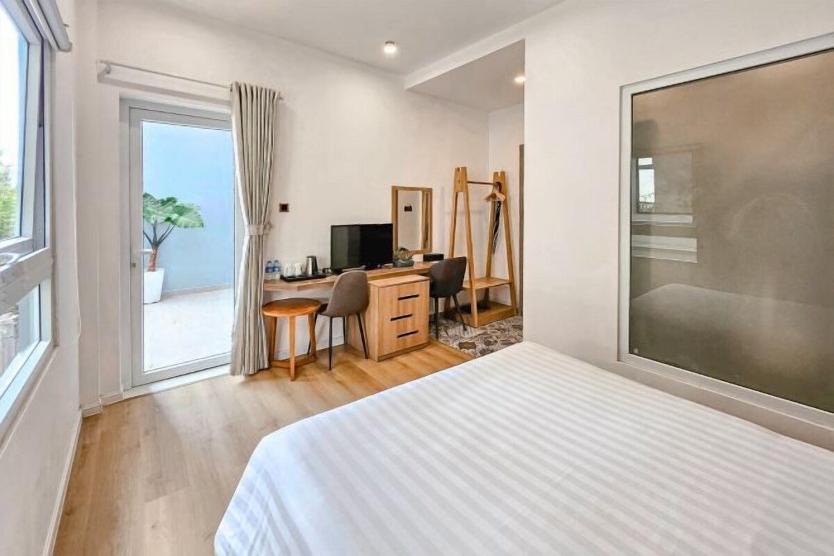 A bedroom with a bed, a desk, a chair, a television, and a large window.
