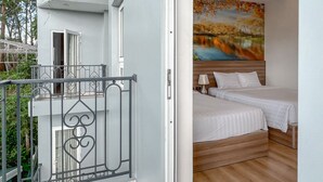 A hotel room with a balcony, a bed with white bedding, a painting on the wall, and a wooden floor. -  NATURE LAND 2 - Song Anh Hotel Dalat (Xuan Huong - Da Lat)