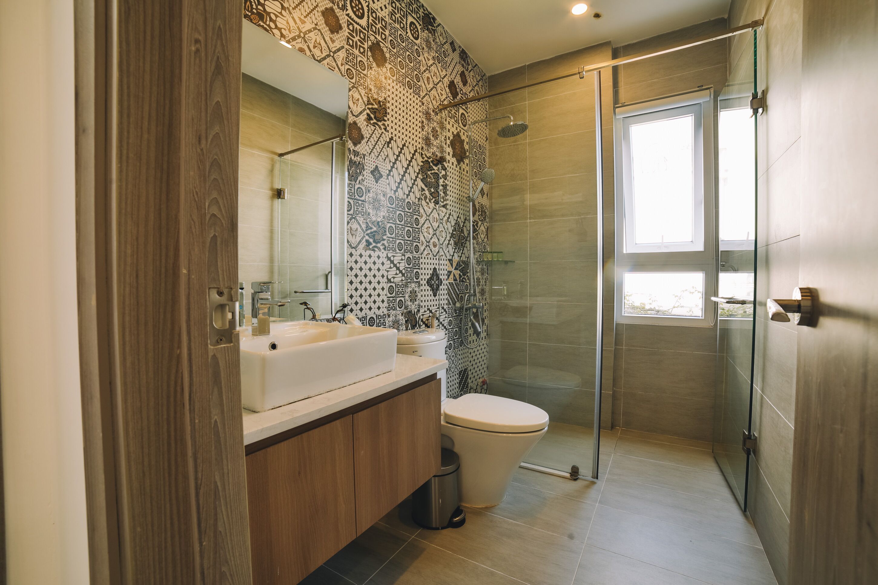 Un baño moderno con tocador de madera, un lavabo blanco, un inodoro y una cabina de ducha de vidrio.