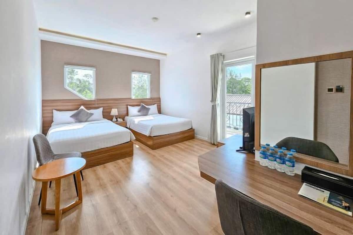 A hotel room with two beds, a desk with water bottles, a chair, and a large mirror.