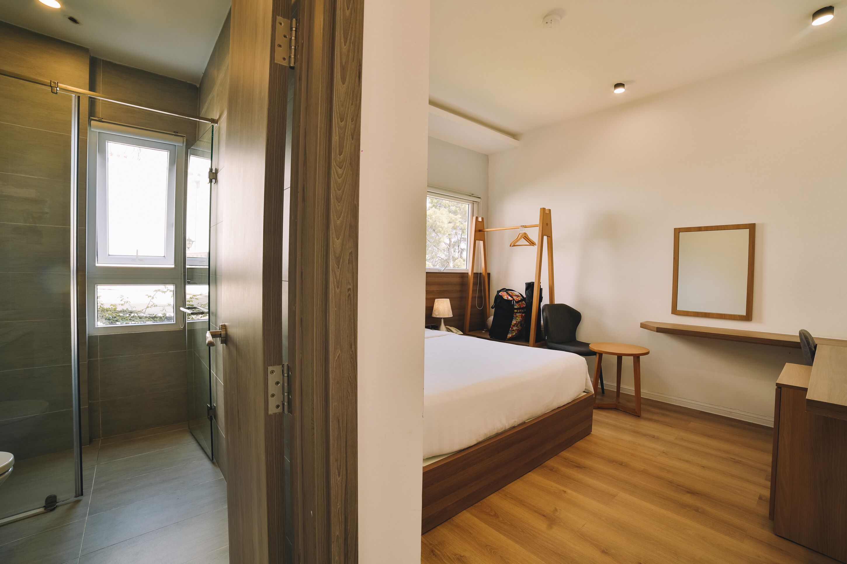 A modern hotel room with a shower, a bed, a desk, and a window.