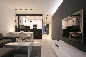 Uma sala de estar moderna com um sofá, mesa de centro e área de jantar. Cozinha visível ao fundo, com um espelho grande e luminárias pendentes.