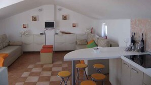 A compact living space with a kitchenette, a dining area with stools, a sofa, and a TV mounted on the wall. - Studio with sea view and air conditioning. (Rovinj)