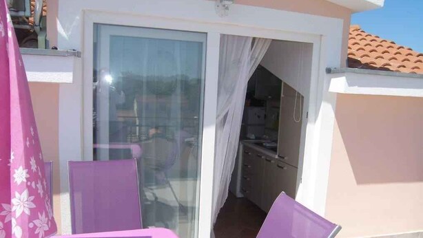A balcony with a table and chairs, a sliding glass door leading to a kitchen, and a yellow object on the ground. - Studio with sea view and air conditioning. (Rovinj)