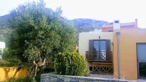 A building with a stone wall, a wooden balcony, and a large tree. - Villa Paradise (Agios Nikolaos)