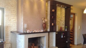 A fireplace with a stone surround, a shelf with decorative items, and a staircase in the background. - Villa Paradise (Agios Nikolaos)