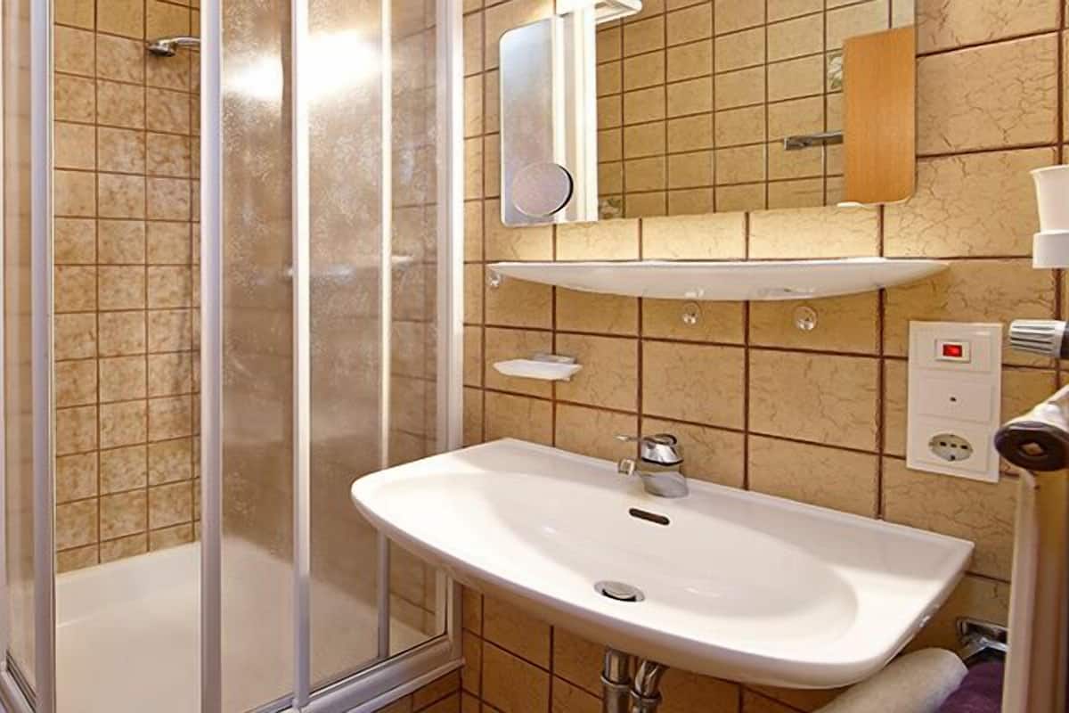 A bathroom with a toilet, shower, sink, and a shelf with towels.