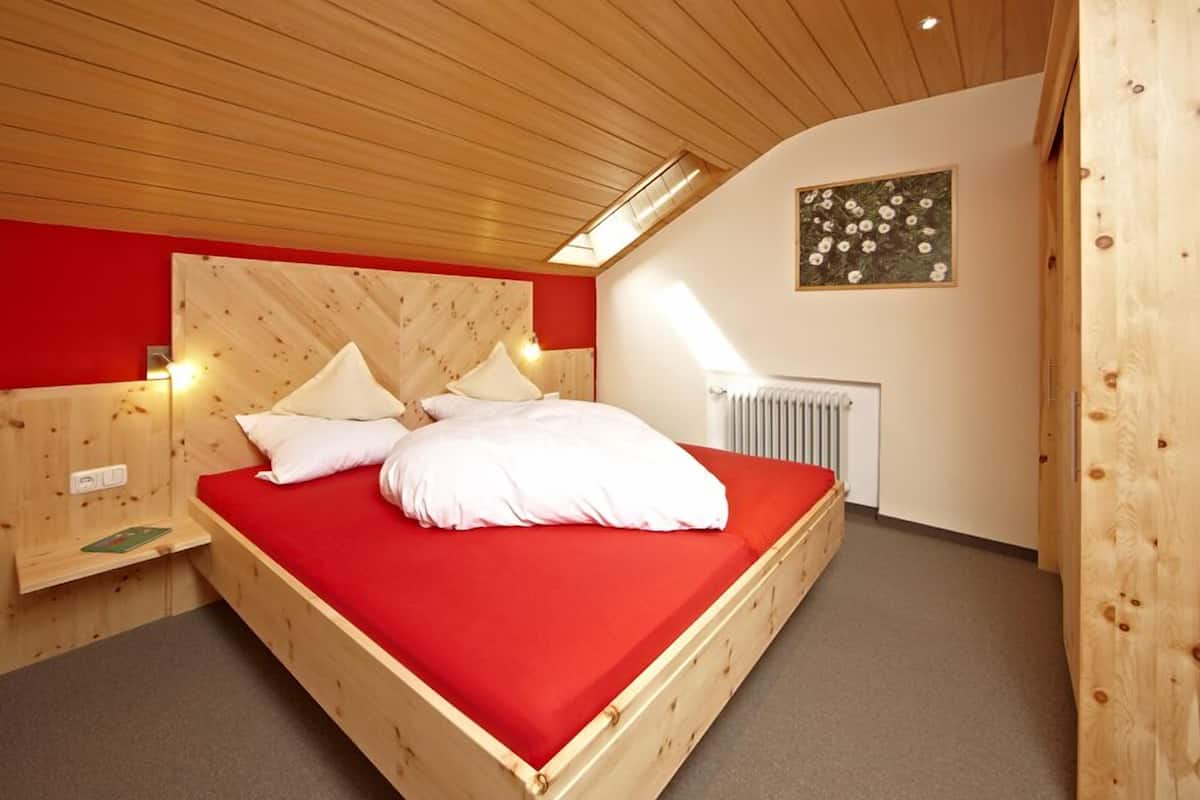 A wooden bed with a red mattress in a room with wooden walls and a sloped ceiling.