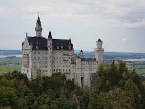 A large, historic castle with multiple towers and a prominent central building, surrounded by lush greenery and a scenic landscape. - Gästehaus Alpina (Bad Kohlgrub)