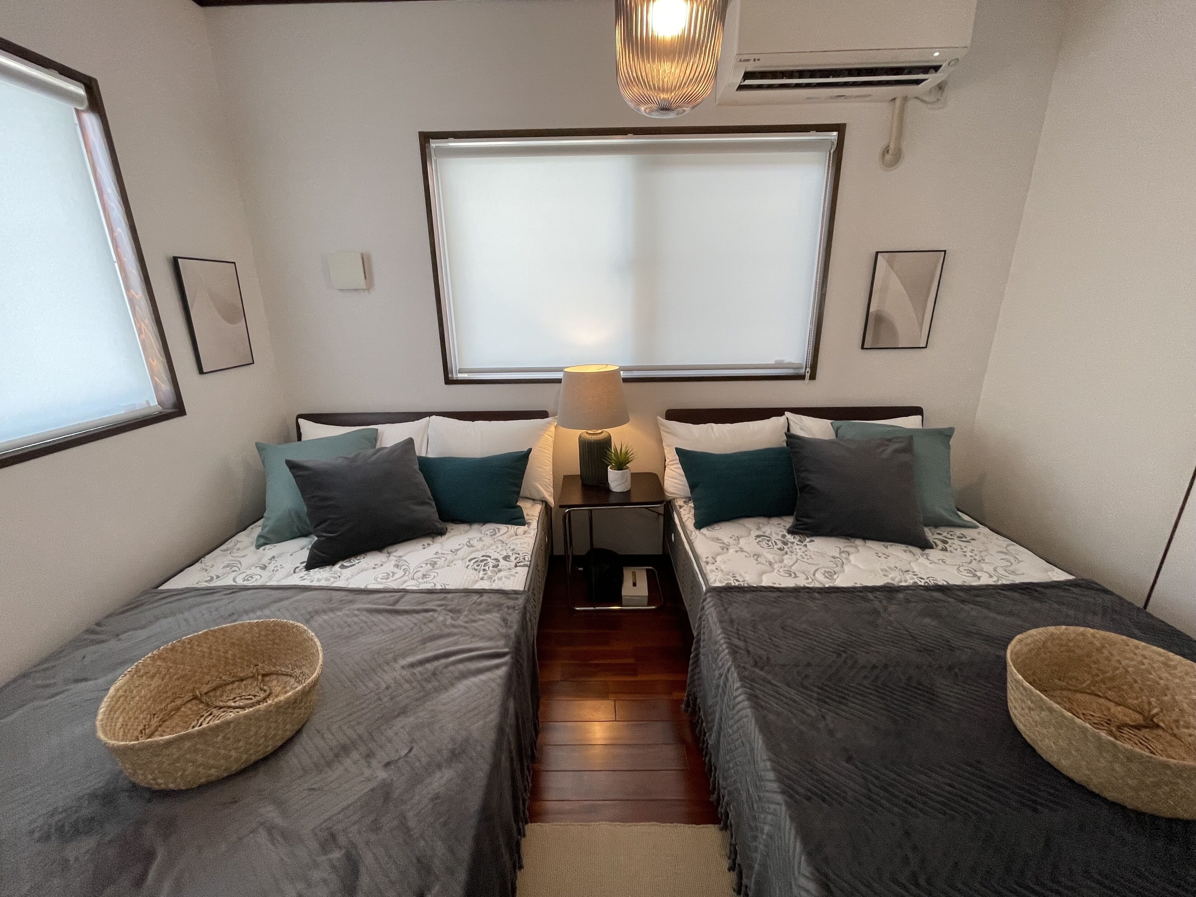 A compact bedroom with two beds, a bedside table with a lamp, and a small window.