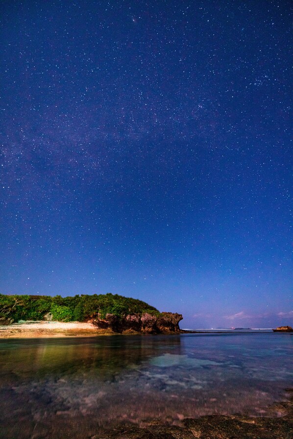 A night sky filled with stars over a coastal landscape with clear waters reflecting the sky. - Ocean view terrace BISE (Motobu)