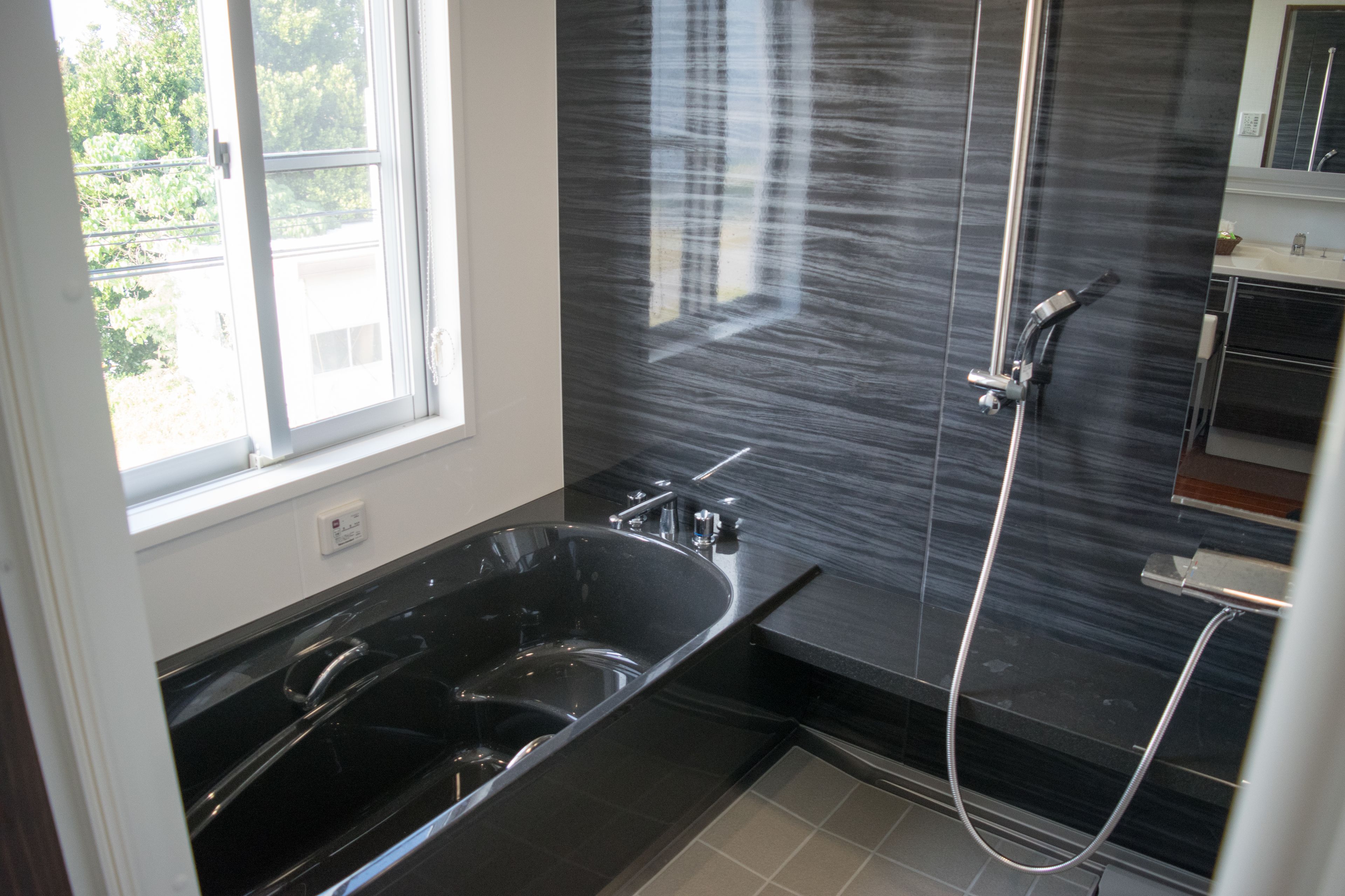 Een moderne badkamer met een zwart bad, een douche en een raam dat natuurlijk licht binnenlaat.