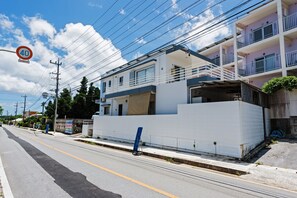 A modern building with a white facade, a balcony, and a visible garage door. - Ocean view terrace BISE (Motobu)