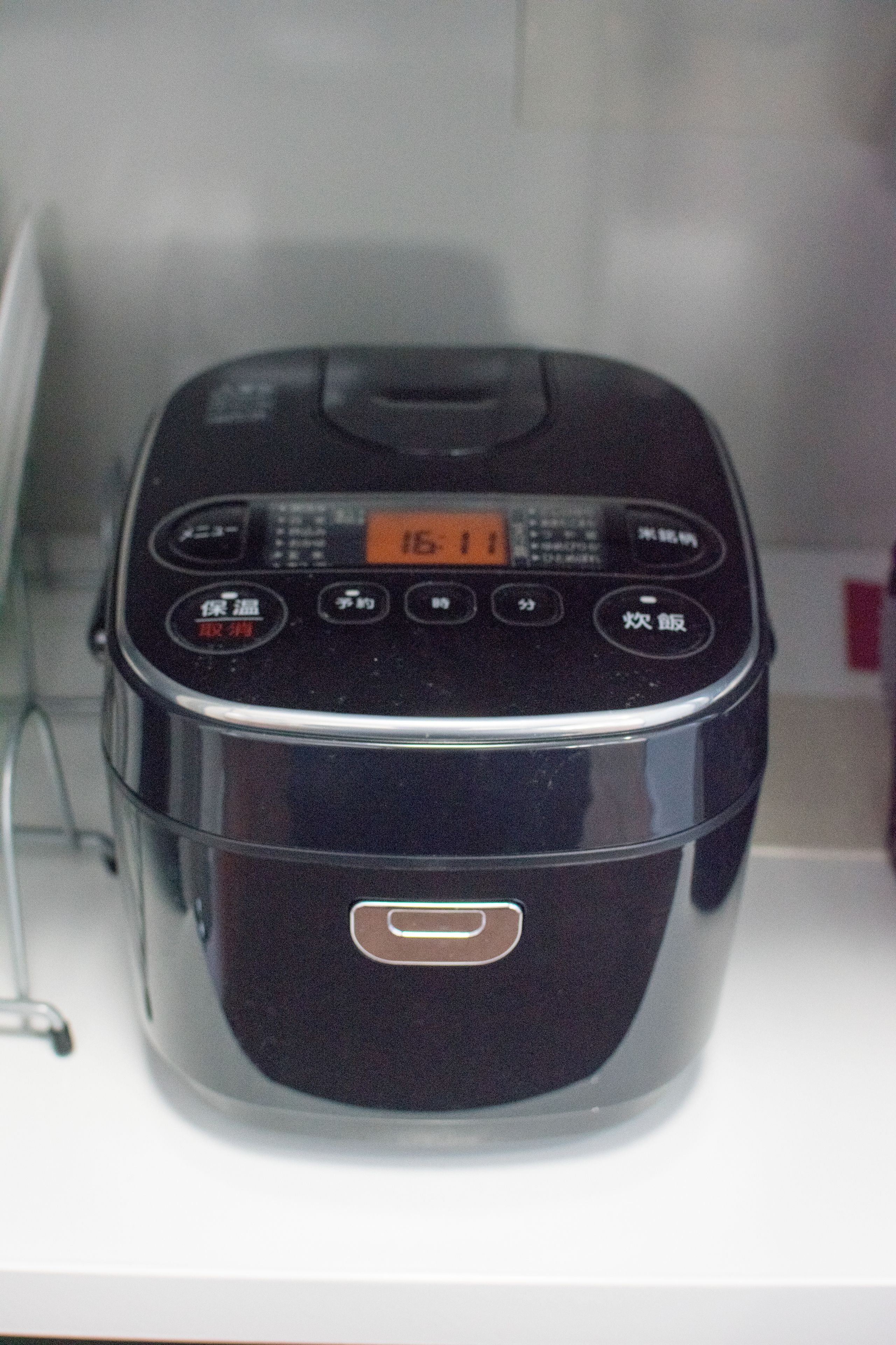 A black rice cooker with a digital display and buttons, placed on a white surface.