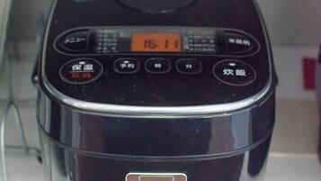 A black rice cooker with a digital display and buttons, placed on a white surface.