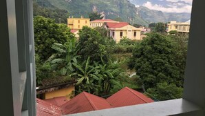 A view from a balcony overlooking a residential area with houses, lush greenery, and mountains in the background. - Cao Nguyen Guesthouse (Yen Minh)