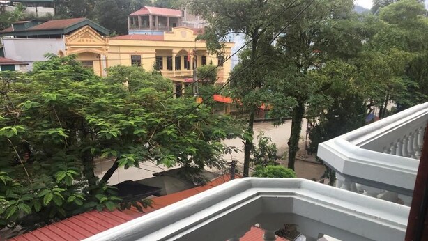 A balcony with a white balustrade overlooking a residential area with trees and buildings. - Cao Nguyen Guesthouse (Yen Minh)