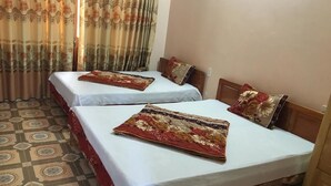 A hotel room with two beds, each with a patterned bedspread and matching pillows. The room has patterned floor tiles and a curtain with a floral design. - Cao Nguyen Guesthouse (Yen Minh)