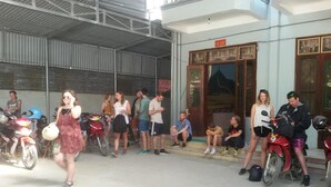 A covered outdoor area with a building entrance, people standing and sitting, and motorcycles parked nearby. - Cao Nguyen Guesthouse (Yen Minh)
