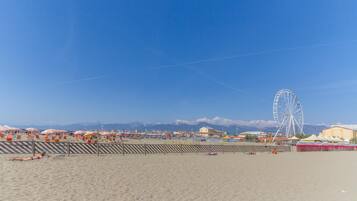 Une plage avec une grande roue en arrière-plan, un ciel dégagé et un horizon montagneux.