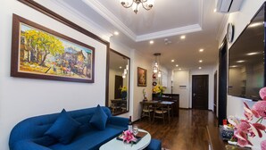 A modern living room with a blue sofa, a dining table, and a kitchen area visible in the background. - Hanoi Central Hotel & Residences (Hanoi)