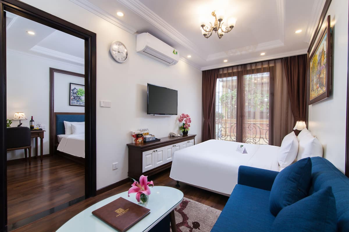 A hotel room with a bed, a sofa, a TV, a desk, and a window with curtains.