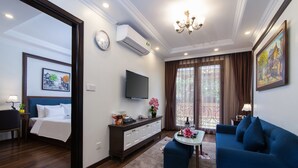 A modern hotel room with a bed, a sofa, a TV, a dining area, and a balcony with curtains. - Hanoi Central Hotel & Residences (Hanoi)