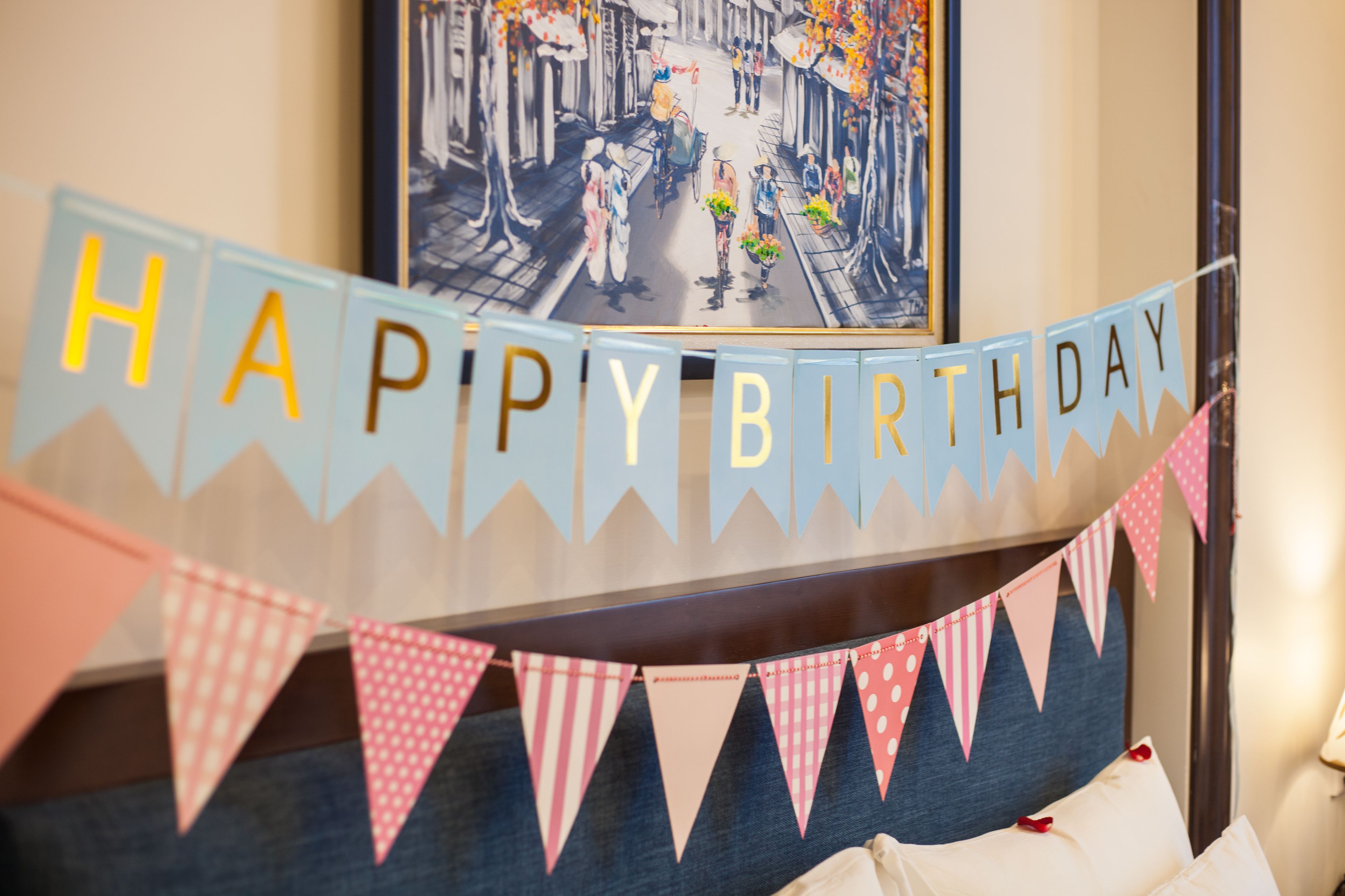 A room with a bed, a 'HAPPY BIRTHDAY' banner, and a framed picture on the wall.