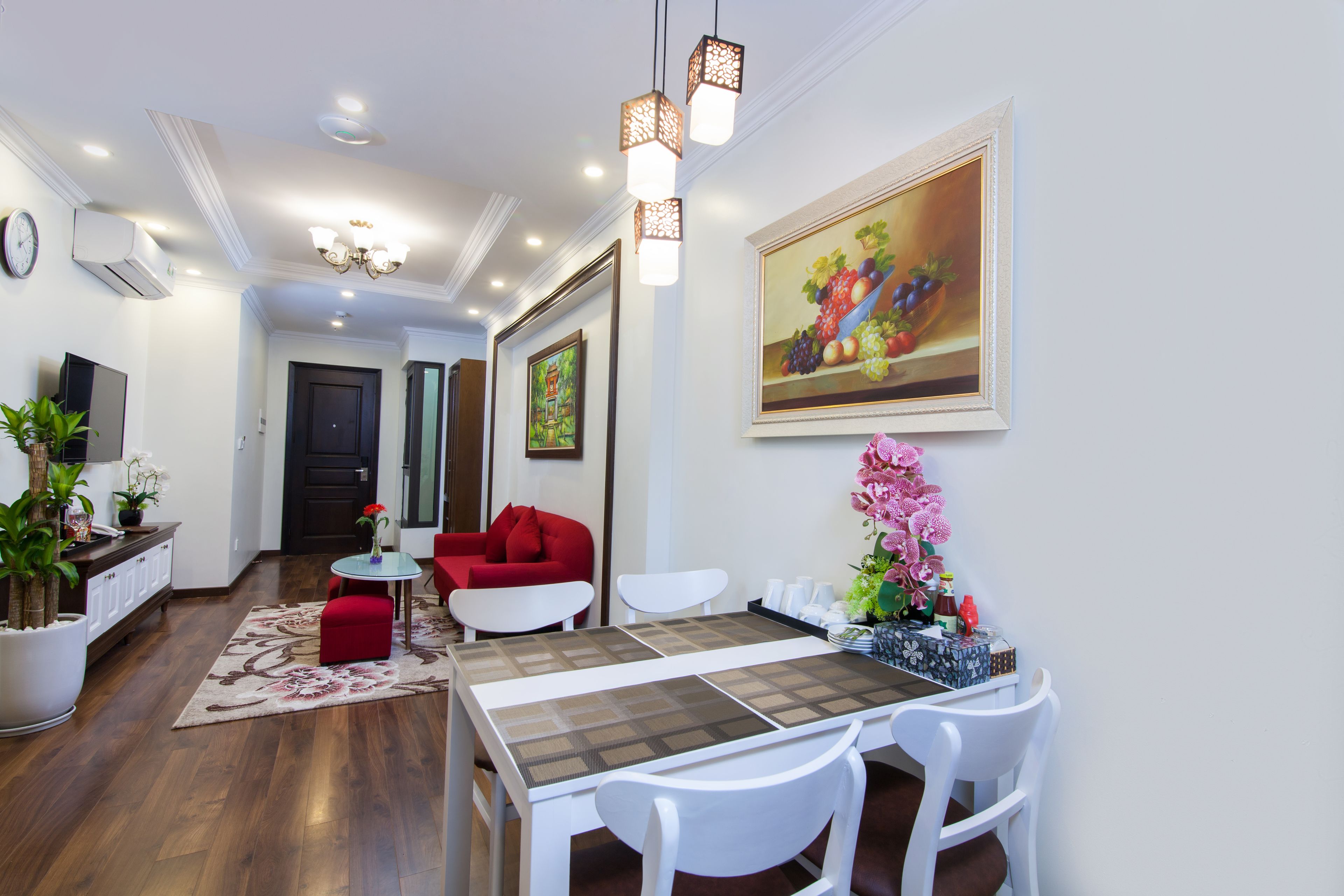 Un salon moderne avec un coin repas, comprenant une table à manger en bois, des chaises blanches, un canapé rouge et un grand tableau accroché au mur.