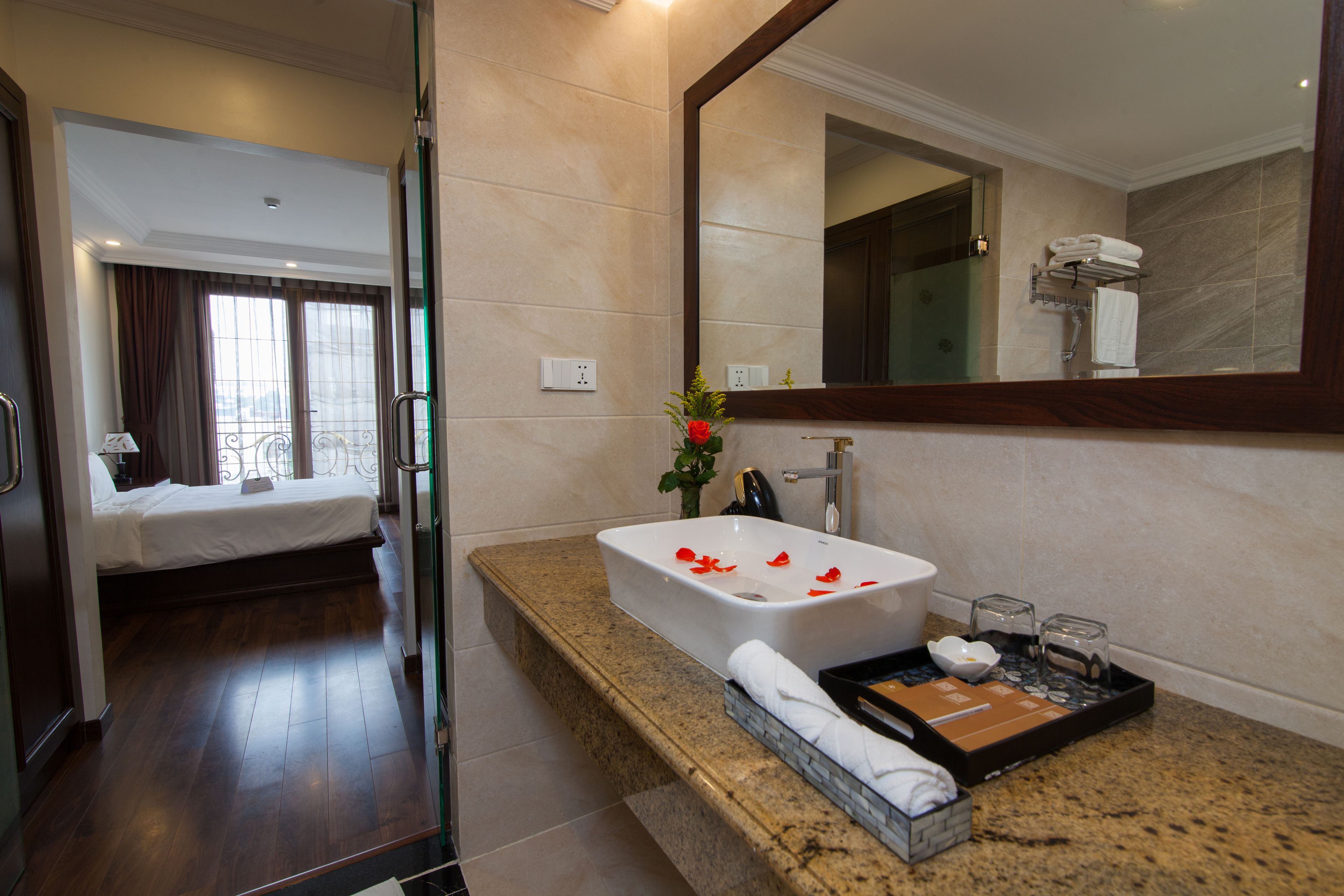 A hotel room with a bed, a bathroom with a large mirror, a sink, and a tray with toiletries.