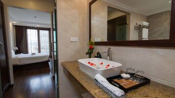 A hotel room with a bed, a bathroom with a large mirror, a sink, and a tray with toiletries.