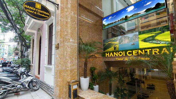 A hotel entrance with a sign reading "HANOI CENTRAL Hotel & Residences," a glass facade, and a view of the street with parked motorcycles. - Hanoi Central Hotel & Residences (Hanoi)