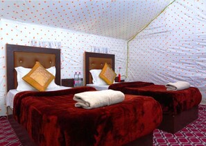 A hotel room with two beds, each with a red blanket and pillows, and a patterned ceiling.
