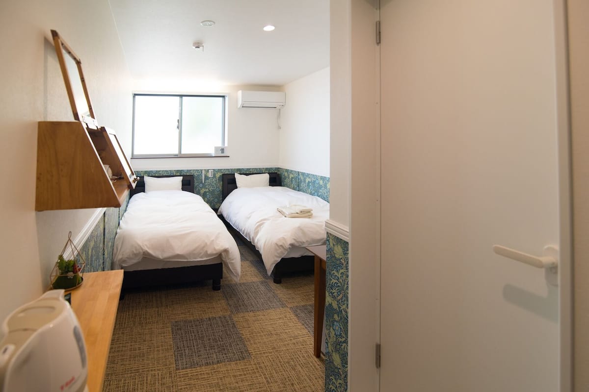 A room with two beds, a wooden desk, a hanging lamp, and a window.