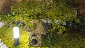 A stone lantern with moss and greenery, a small white structure, and a light source. - Kyo-Anthu Inn (Kyoto)