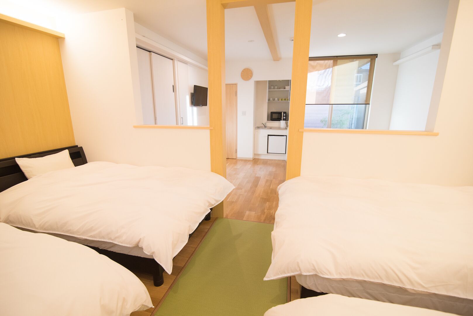A hotel room with three beds, a kitchenette, and a view of the outside.