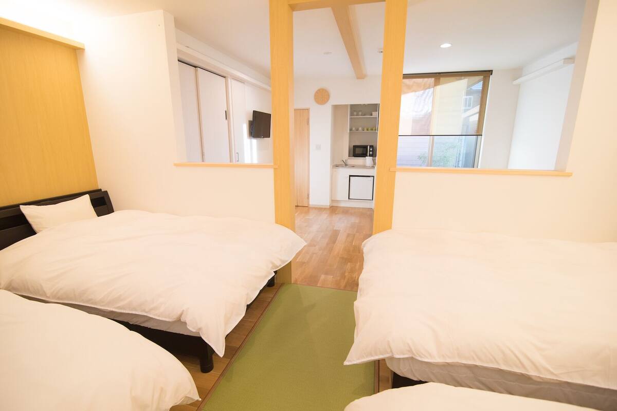 A hotel room with three beds, a kitchenette, and a view of the outside.