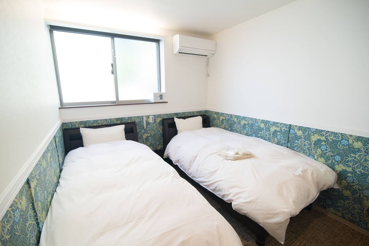 A bedroom with two beds, a window, and an air conditioning unit.