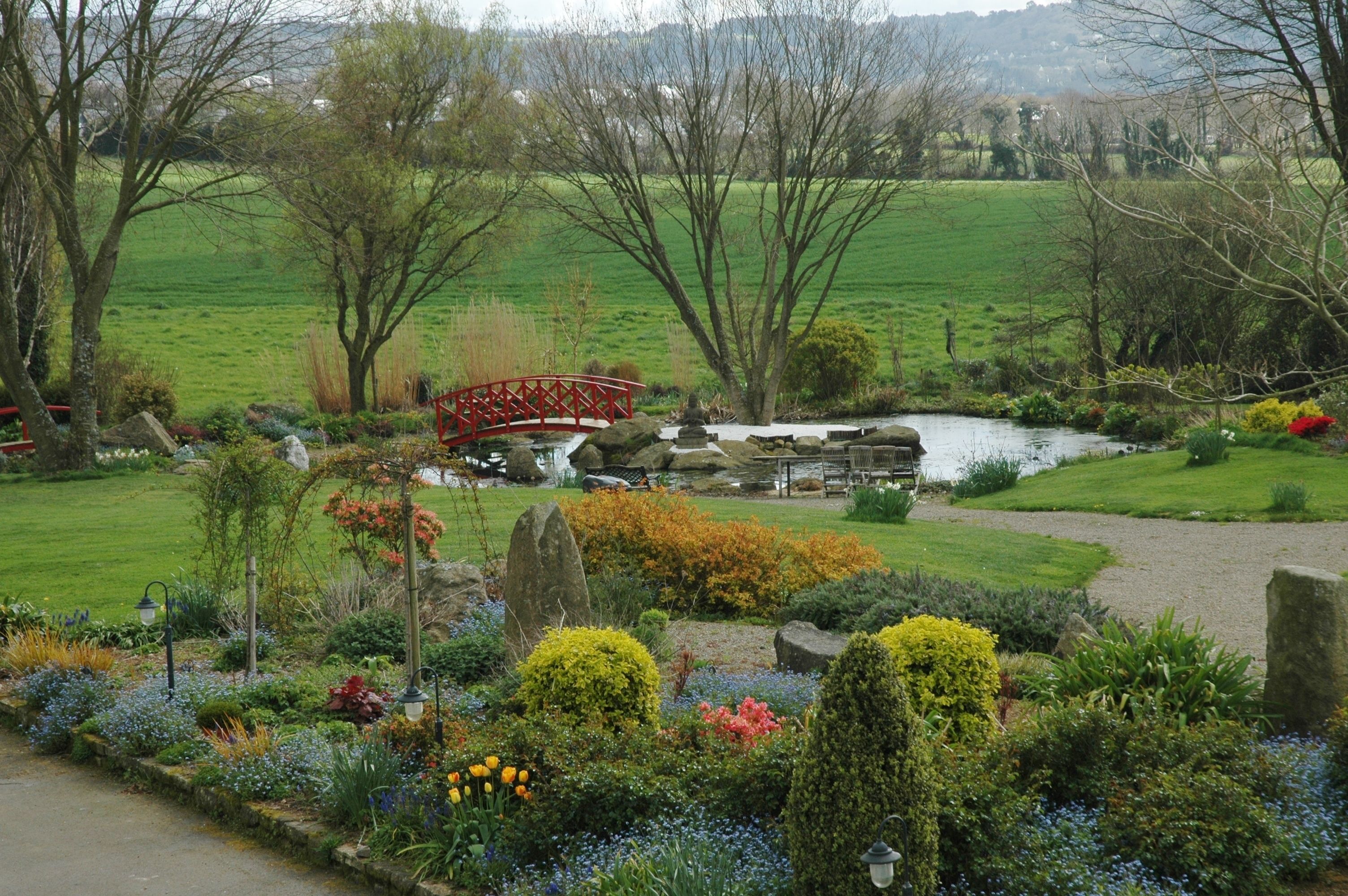 Un jardín con un puente rojo, un estanque y diversas plantas.
