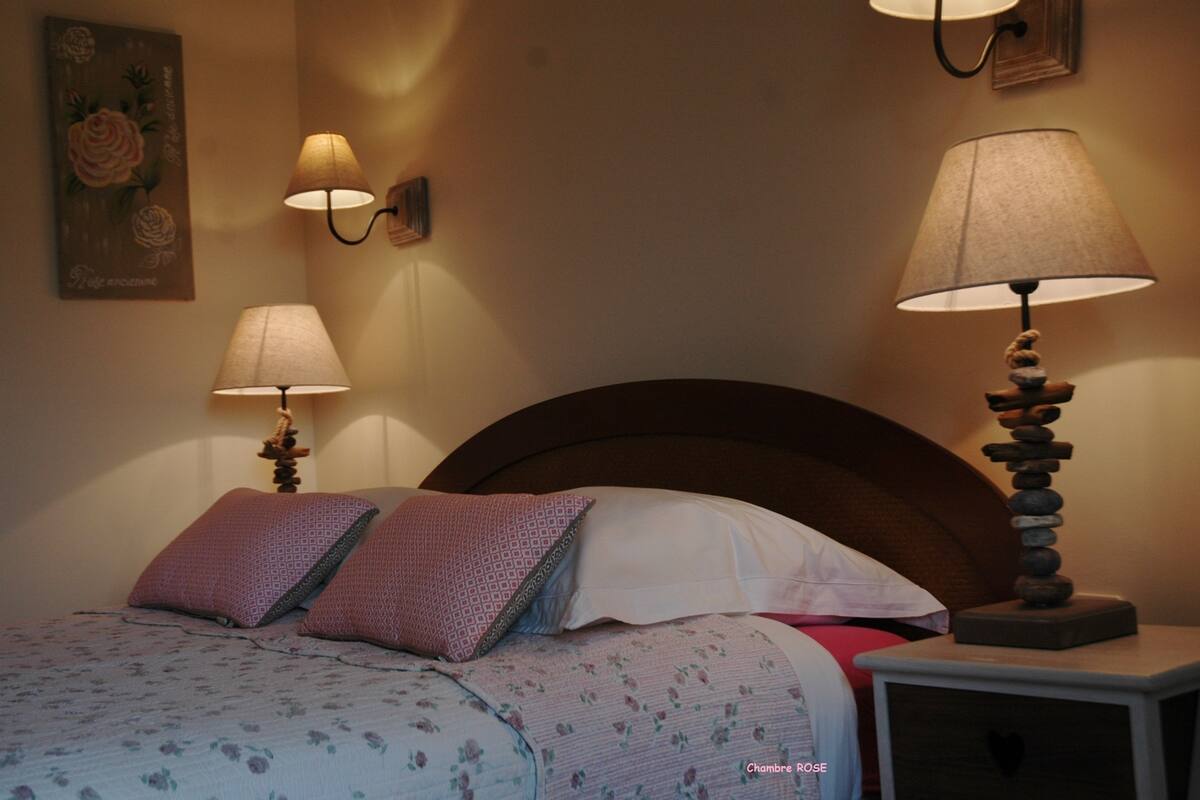 A bedroom with a bed, two wall-mounted lamps, a bedside table with a lamp, and a painting on the wall.