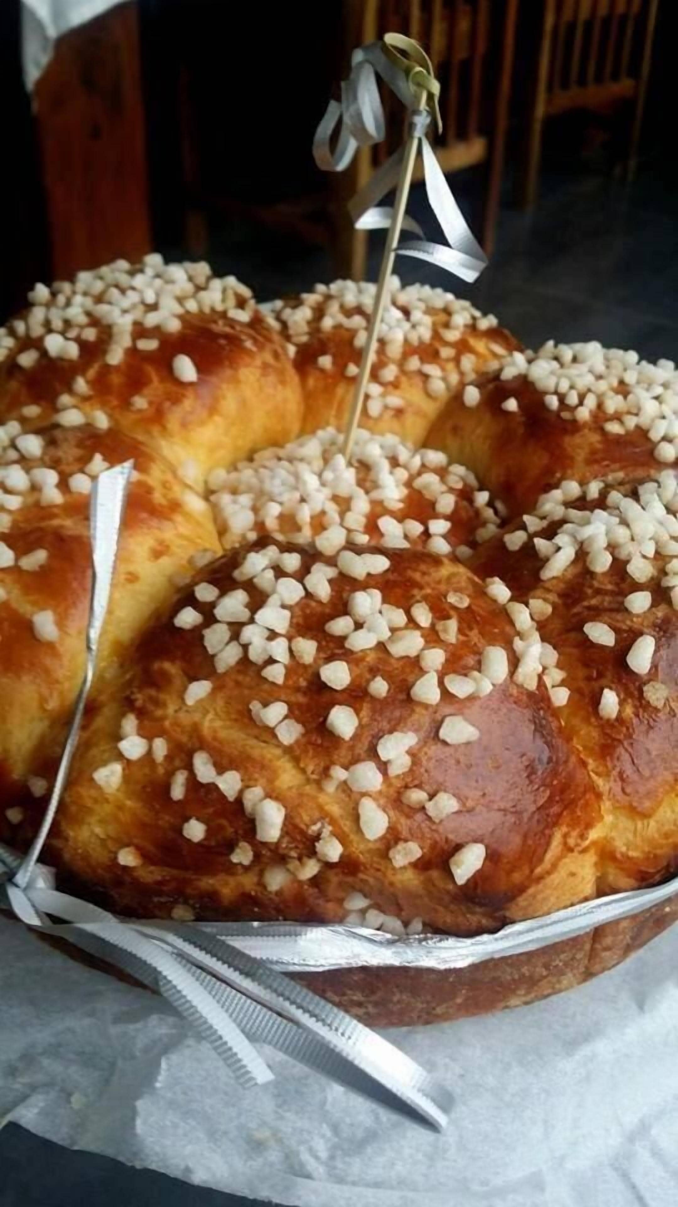 A round tray of bread rolls topped with white sugar pearls, placed on a reflective surface.
