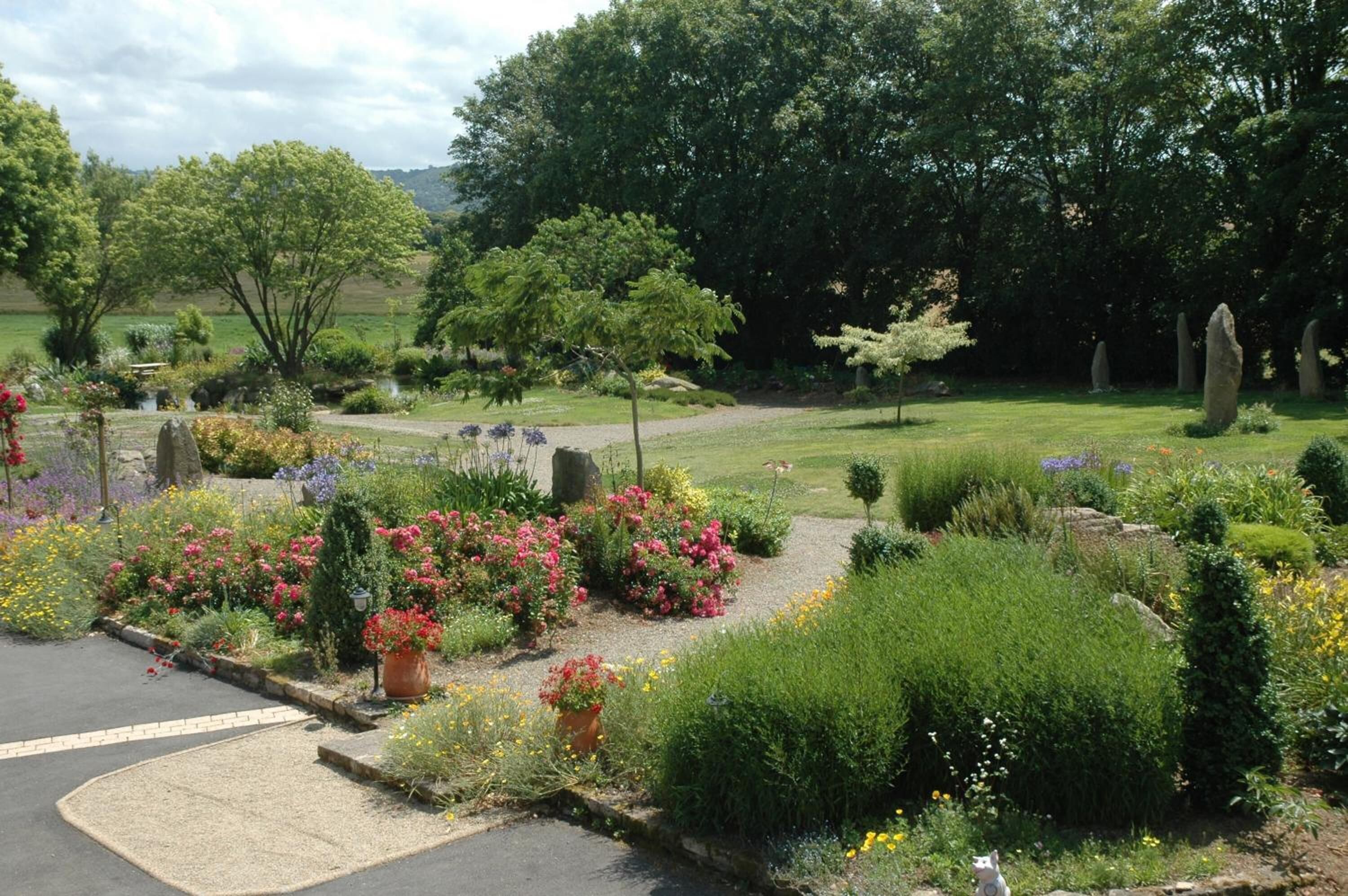 Ein angelegter Garten mit verschiedenen Pflanzen und Blumen, einem gepflasterten Weg und Steinelementen.