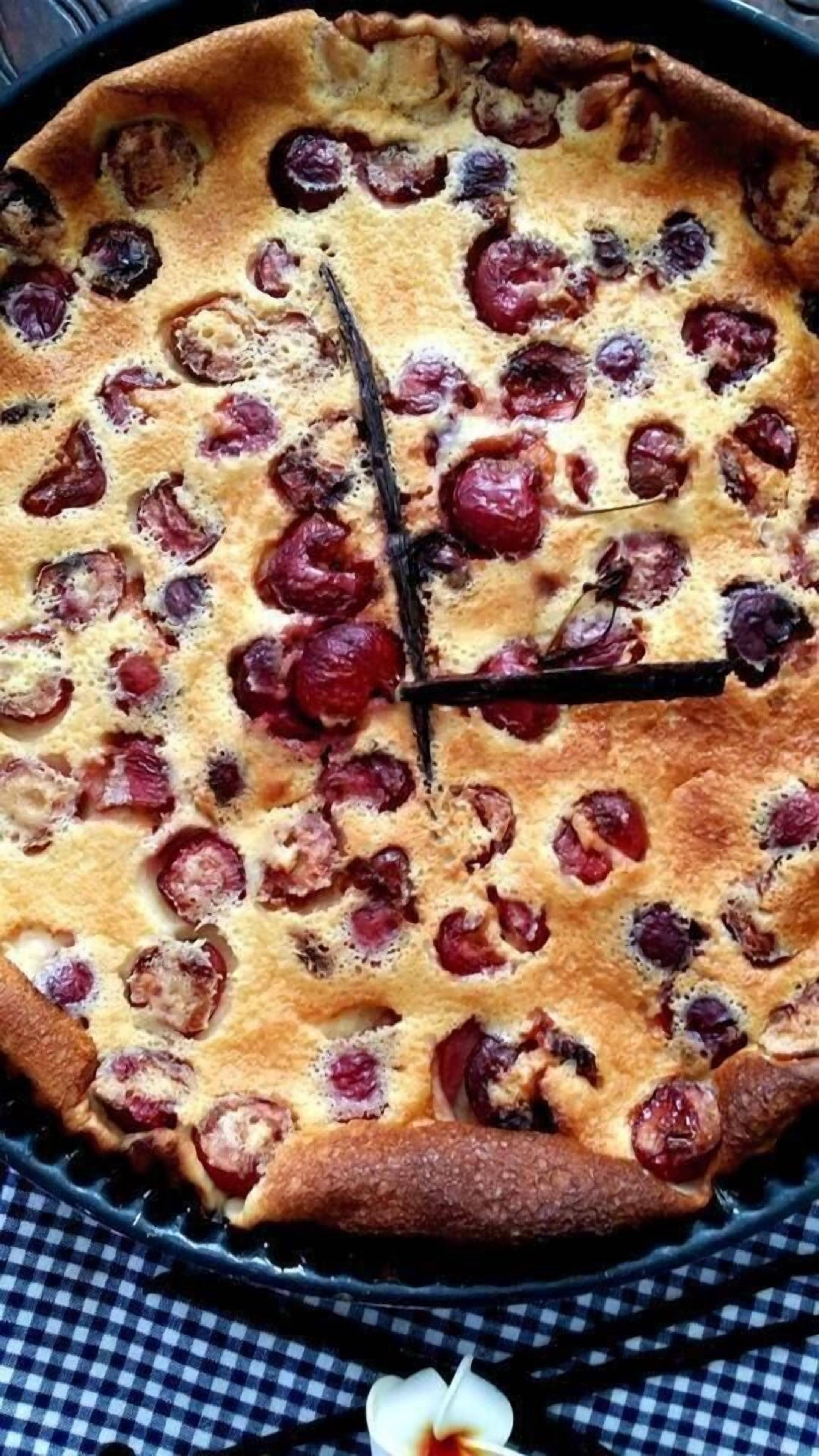 Una tarta redonda de color marrón dorado con trozos de fruta visibles en la parte superior, sobre un mantel a cuadros.